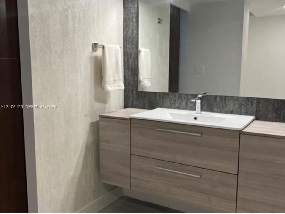 Floating wood-finish vanity with dual storage drawers, integrated white sink, brushed metal hardware, and large frameless mirror