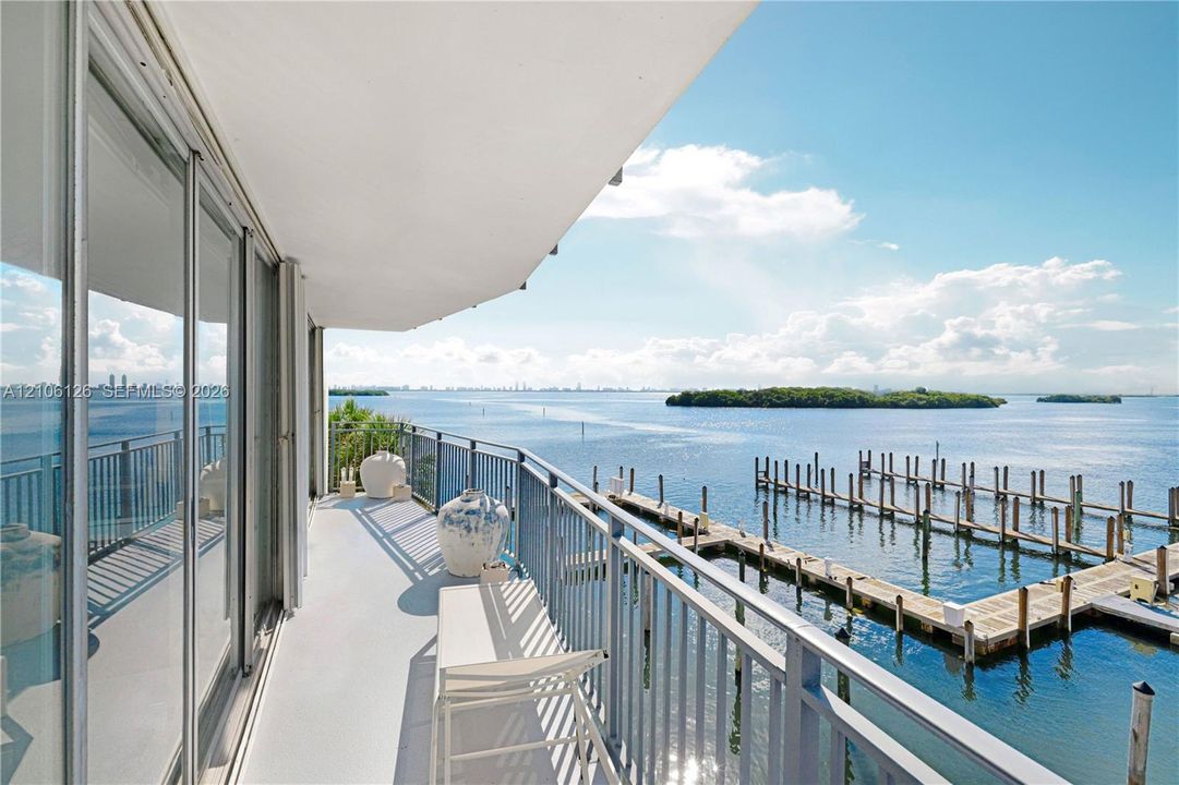 Covered balcony with a protective metal railing, floor-to-ceiling glass sliding doors, and water frontage featuring a private dock system