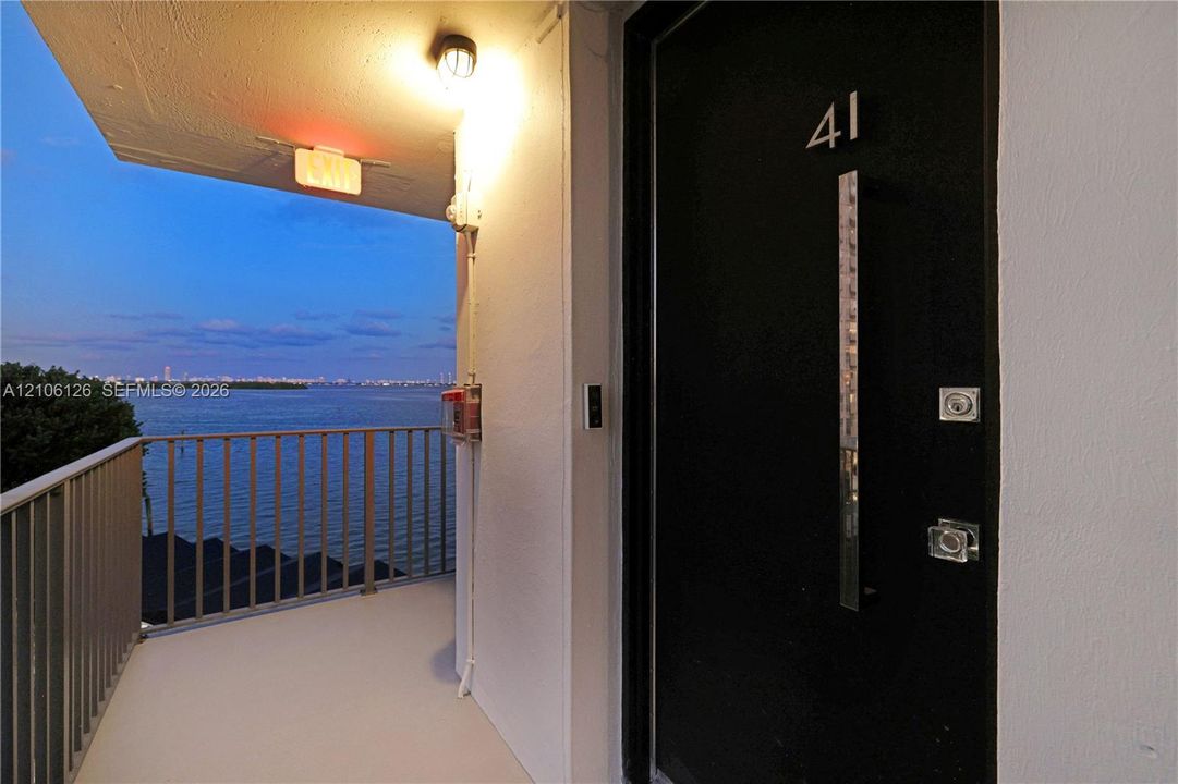 Entrance featuring a black door with a vertical metallic handle and metal railing overlooking the water