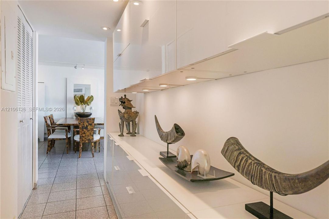 Hallway featuring high-gloss white cabinetry, integrated under-cabinet lighting, and neutral tile flooring
