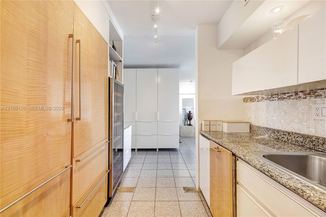 Kitchen featuring floor-to-ceiling wood-veneer cabinetry, integrated wine refrigeration, stone countertops, mosaic tile backsplash, and sleek white upper cabinetry