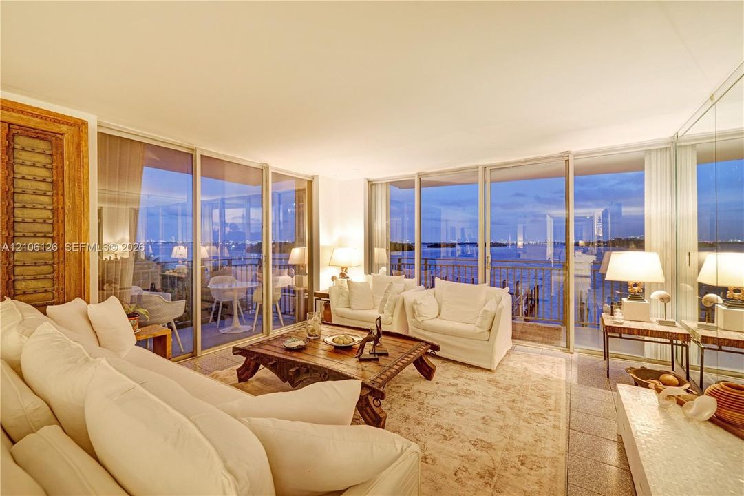 Floor-to-ceiling glass sliding doors, stone tile flooring, mirrored wall paneling, and an expansive exterior balcony