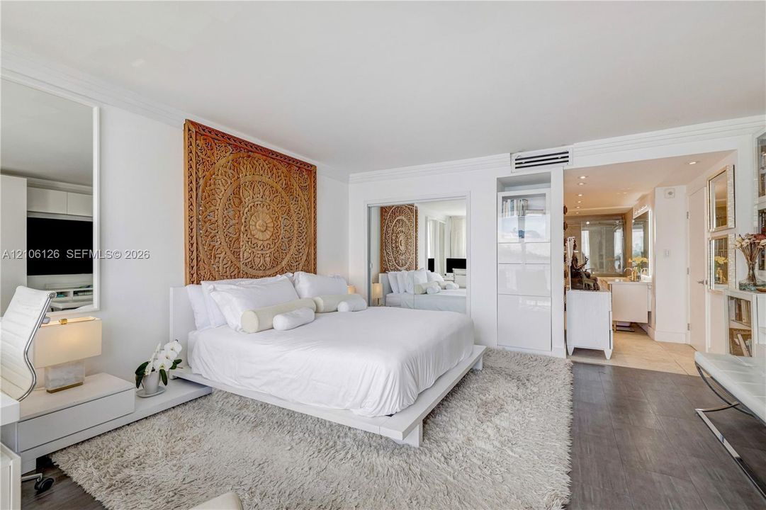 Living space featuring crown molding, wall-mounted air conditioning unit, wood-finish flooring, and mirrored closet doors