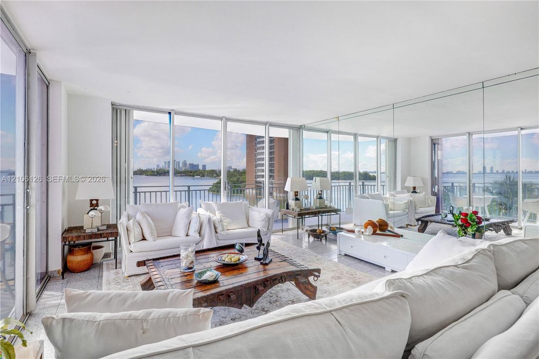 Floor-to-ceiling glass walls, integrated mirrored wall panels, stone-finish flooring, and private balcony access with water backdrop