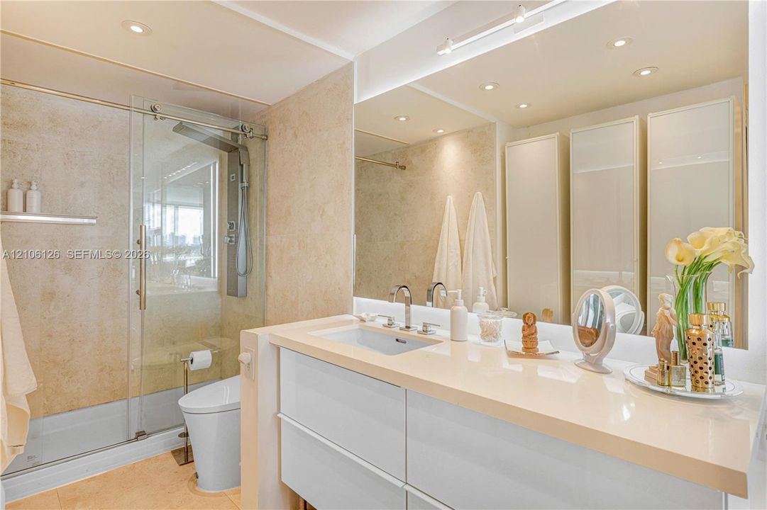 Modern bathroom featuring a wall-mounted floating vanity with a stone countertop, dual chrome faucets, a glass-enclosed walk-in shower with stone tile wall surfacing, and floor-to-ceiling built-in cabinetry