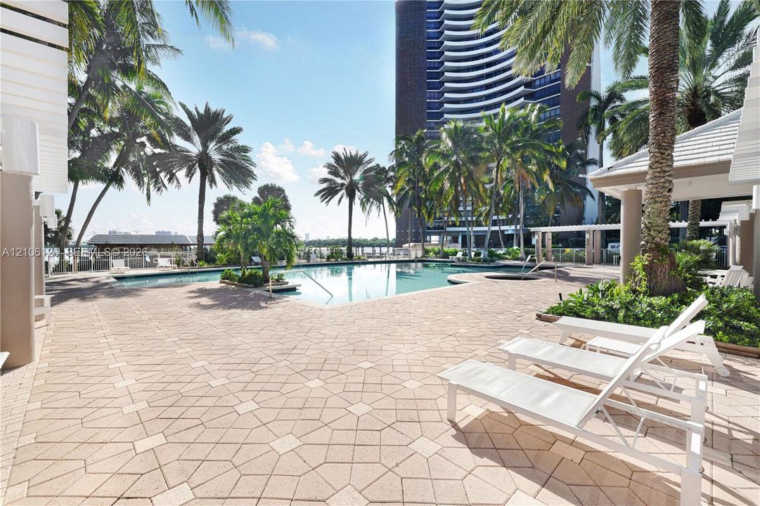 Swimming pool with integrated spa, concrete paver patio, and mature palm trees