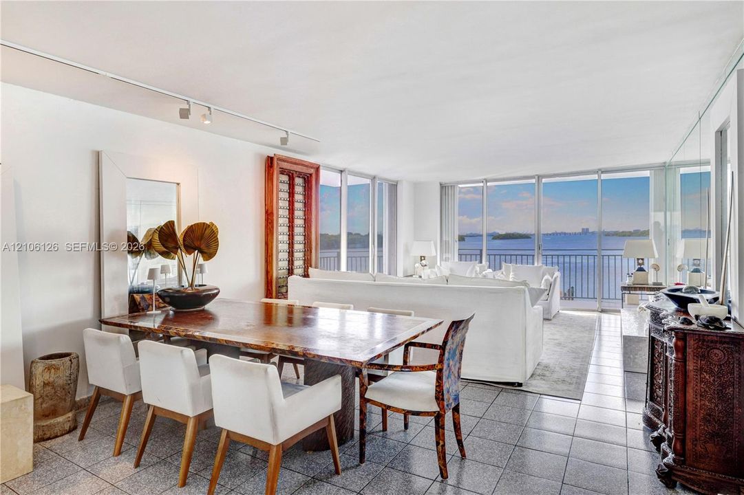 Open-concept living space featuring floor-to-ceiling windows, panoramic water scenery, polished stone-tile flooring, and adjustable ceiling-mounted track lighting