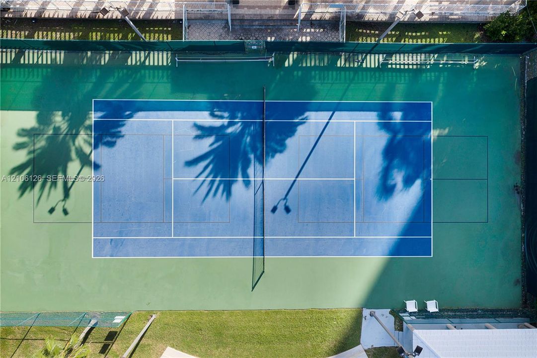 Tennis court featuring a hard surface with green and blue court markings, perimeter fencing, and integrated lighting fixtures