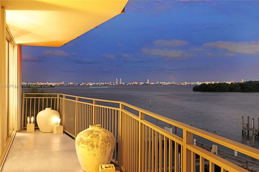 Private balcony featuring a metallic railing, a hard-surface deck, and expansive water frontage with a city skyline backdrop