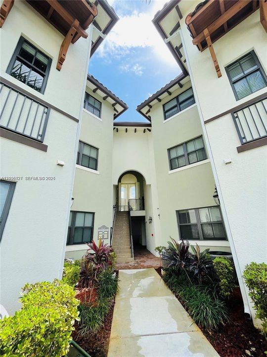 Exterior facade featuring stucco siding, multi-level balconies with metal railings, decorative wood corbels, and a concrete paver walkway