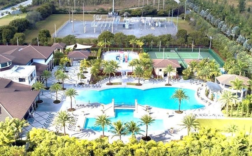 Community amenity complex featuring a large swimming pool, tennis court, outdoor pavilion, and landscaped grounds with mature palm trees