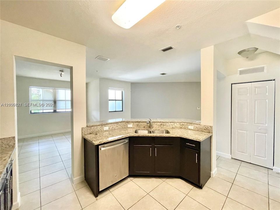 Kitchen area featuring dark cabinetry, stone-surface countertops, dual-basin stainless steel sink, stainless steel dishwasher, and tile flooring