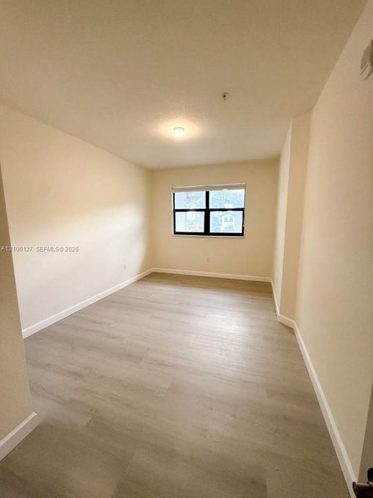 Neutral interior room featuring wood-finish flooring, a grid-pattern window with a dark frame, and a flush-mount ceiling light