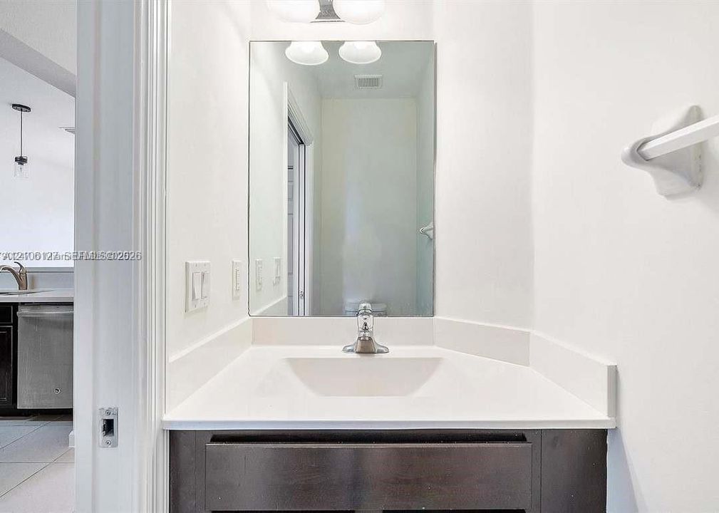 Dark wood vanity cabinet with a white integrated sink, polished chrome faucet, rectangular wall-mounted mirror, and wall-mounted towel bar