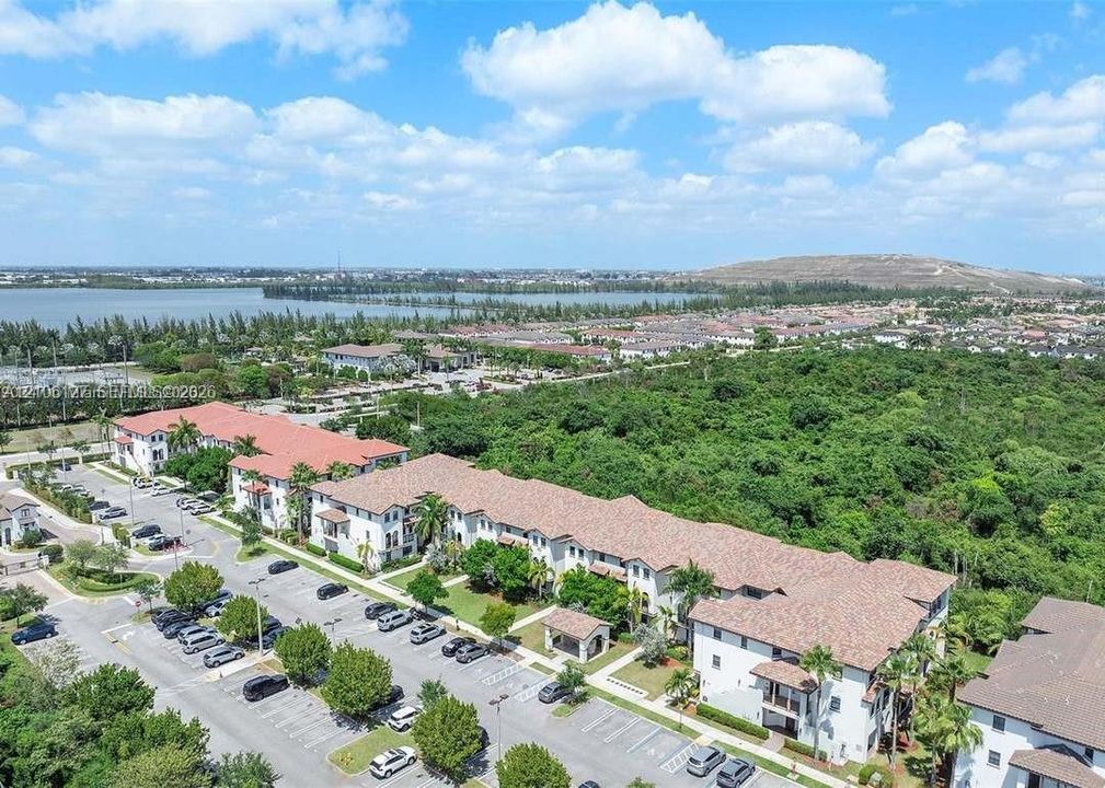 Aerial perspective of a multi-story residential complex featuring barrel tile roofing, white stucco exteriors, and surface parking