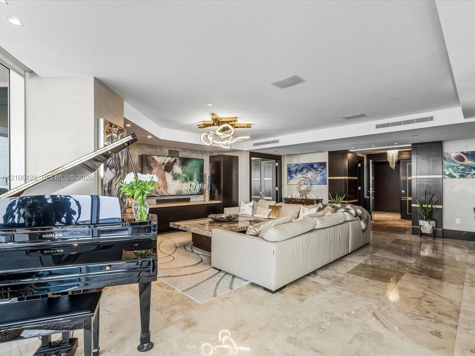 Open-concept living space featuring polished stone flooring, custom dark wood-veneer cabinetry, recessed lighting, and a modern sculptural chandelier