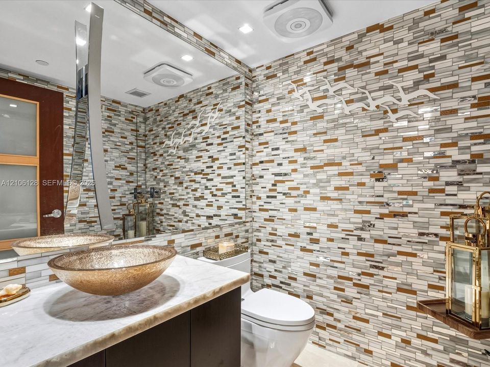 Bathroom featuring a stone vanity top, glass vessel sink, large wall-mounted mirror, and decorative mosaic tile accent wall