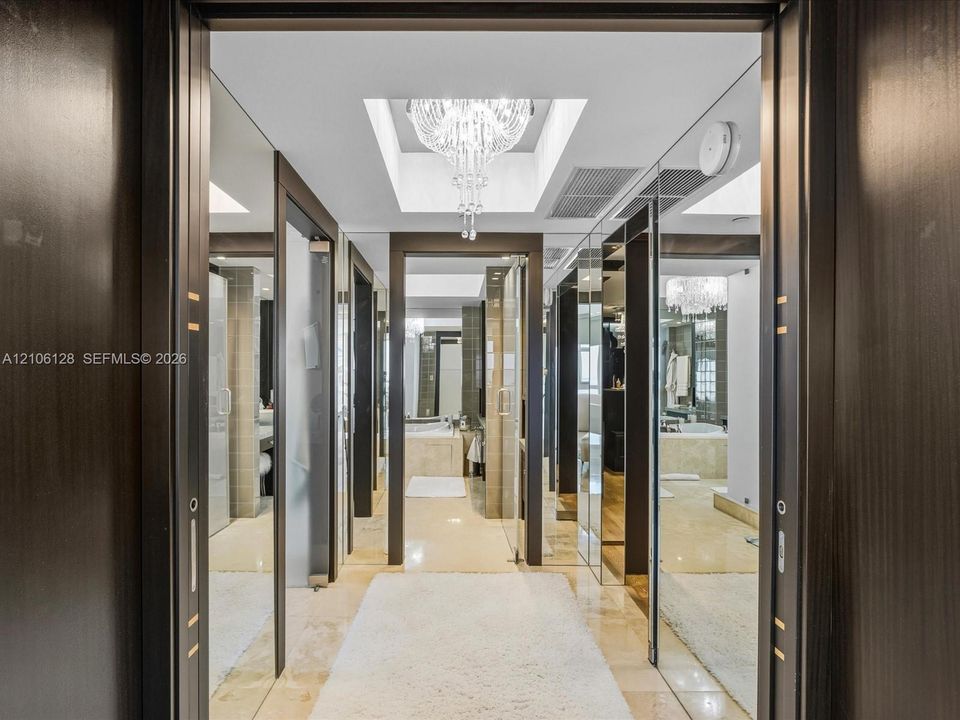 High-gloss dark wood doorways with metal inlay, full-length mirror paneling, recessed lighting, and a crystal chandelier