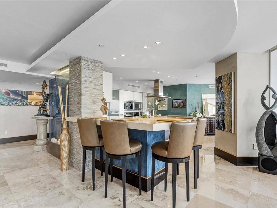 Custom kitchen island with a stone-finish countertop and blue cabinetry, textured stone accent pillar, recessed ceiling lighting, and polished stone flooring