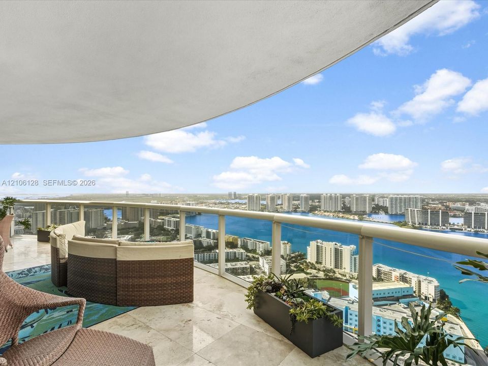 Curved covered balcony featuring stone flooring and a glass railing with metal trim