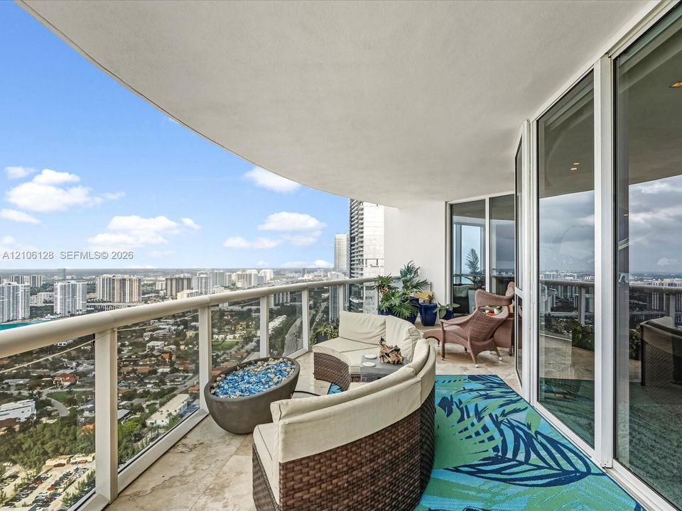 Curved balcony featuring natural stone flooring, glass railing, and floor-to-ceiling glass doors