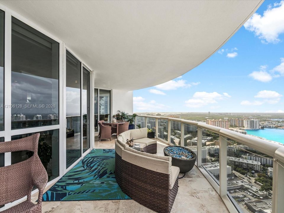 Curved private balcony featuring stone flooring, floor-to-ceiling glass doors, and a glass-paneled railing