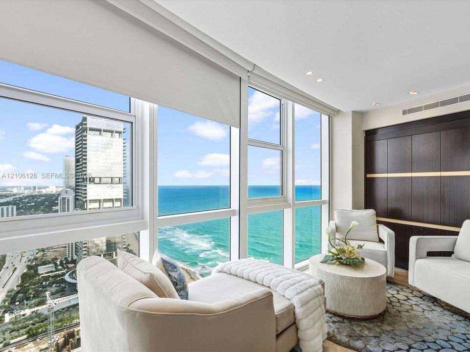 Floor-to-ceiling windows featuring ocean and city panoramas, recessed lighting, and dark wood-finish built-in cabinetry with metallic accents