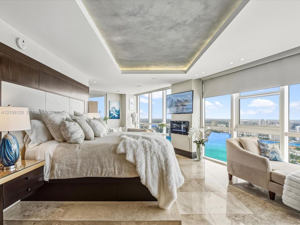 Floor-to-ceiling windows, stone tile flooring, built-in recessed ceiling lighting with textured inlay, and wall-mounted electric fireplace
