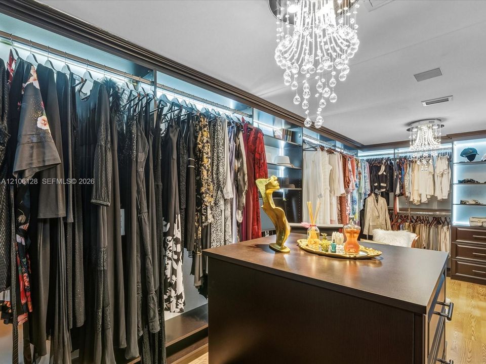 Custom walk-in closet featuring extensive dark-finish built-in shelving, integrated cabinet lighting, a central storage island, and two tiered crystal chandeliers