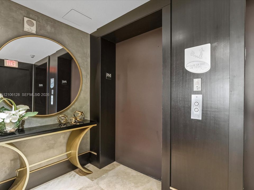 Elevator lobby featuring custom dark wood door surround, textured concrete-style wall finish, and stone flooring