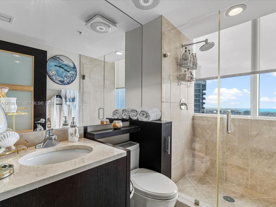Bathroom featuring a stone-surface vanity with an integrated undermount sink, dark-finish cabinetry, floor-to-ceiling tile shower enclosure, glass partition, and full-width vanity mirror