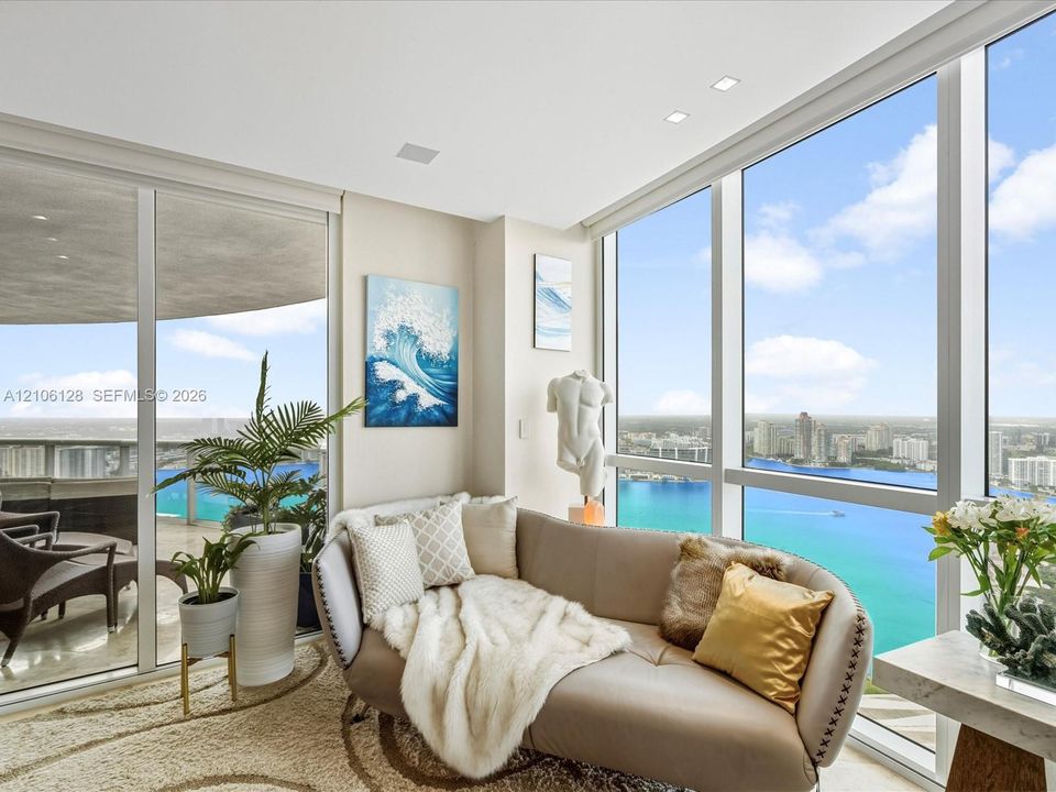 Floor-to-ceiling glass windows, expansive water backdrop, recessed ceiling lighting, sliding glass door, and wraparound balcony