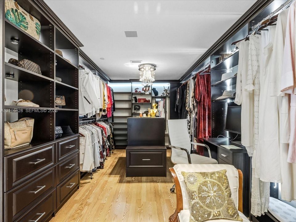 Custom walk-in closet featuring floor-to-ceiling dark wood cabinetry, integrated storage island with drawers, built-in desk workstation, wood-finish flooring, and a crystal chandelier