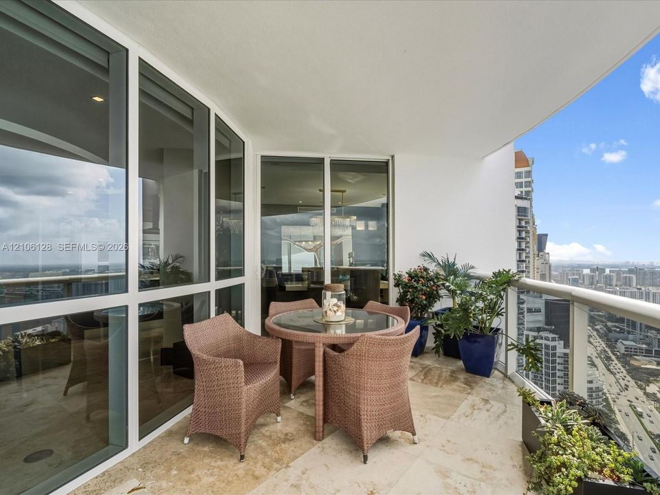 Covered private balcony featuring stone flooring, floor-to-ceiling glass paneling, and glass-and-metal railings