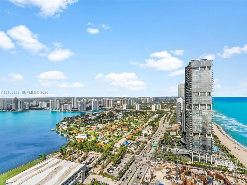 Aerial perspective featuring a high-rise glass tower, direct oceanfront positioning, expansive coastal shoreline, and proximity to regional waterways