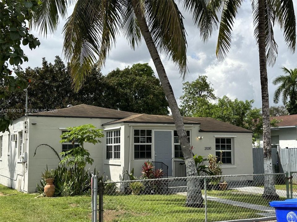 Single-story exterior featuring light-toned masonry, multi-pane windows, a low-pitch roof, and mature palm trees