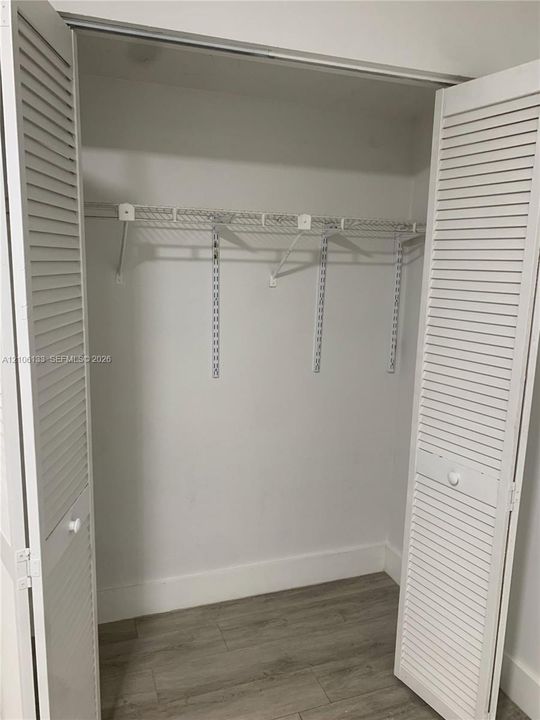 Storage closet featuring dual white louvered bi-fold doors, wood-finish flooring, and integrated wire shelving with a hanging rod