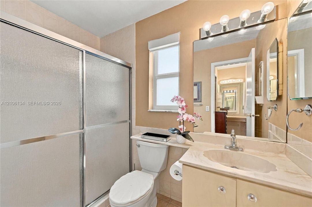 Bathroom featuring a vanity with a stone countertop and integrated sink, chrome faucet, wall-mounted mirror with four-light fixture, and walk-in shower with a sliding glass door