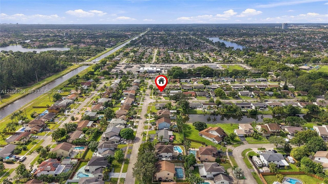 Aerial perspective of a suburban neighborhood featuring a grid street pattern, mature canopy trees, residential parcels, and proximity to regional waterways