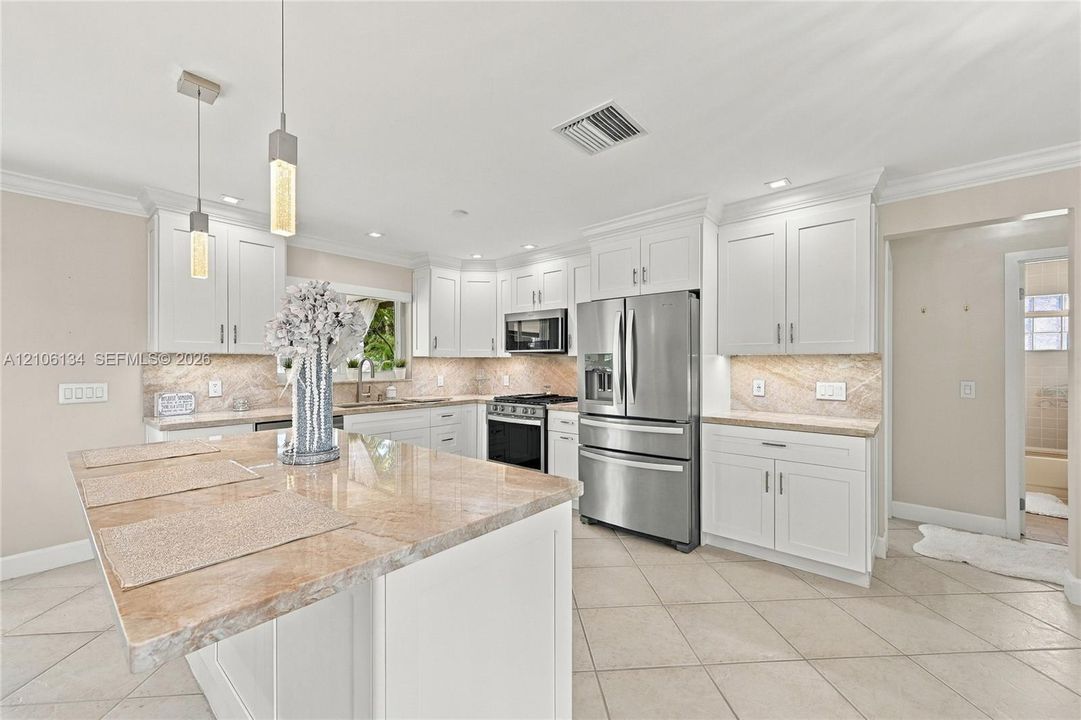 Kitchen featuring white shaker-style cabinetry, stone countertops, central island, stainless steel appliances, and tile flooring