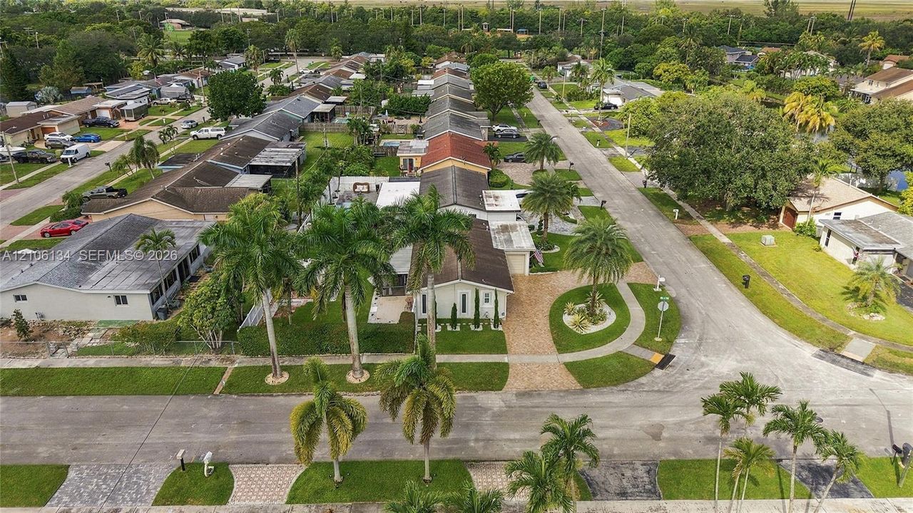 Aerial perspective of the property featuring a paver driveway, mature palm trees, landscaped green space, and residential street access