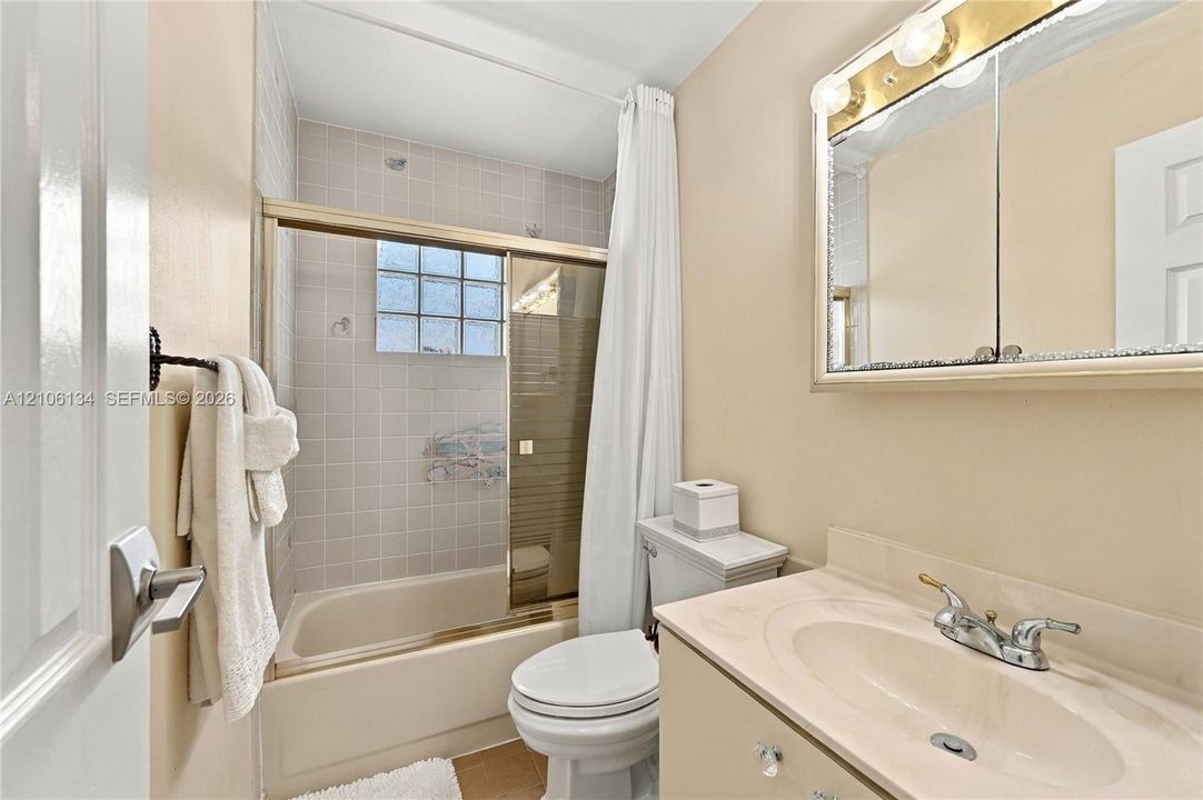 Bathroom featuring a vanity with an integrated basin, a mirrored medicine cabinet with integrated lighting, and a bathtub with a glass sliding enclosure and glass block window