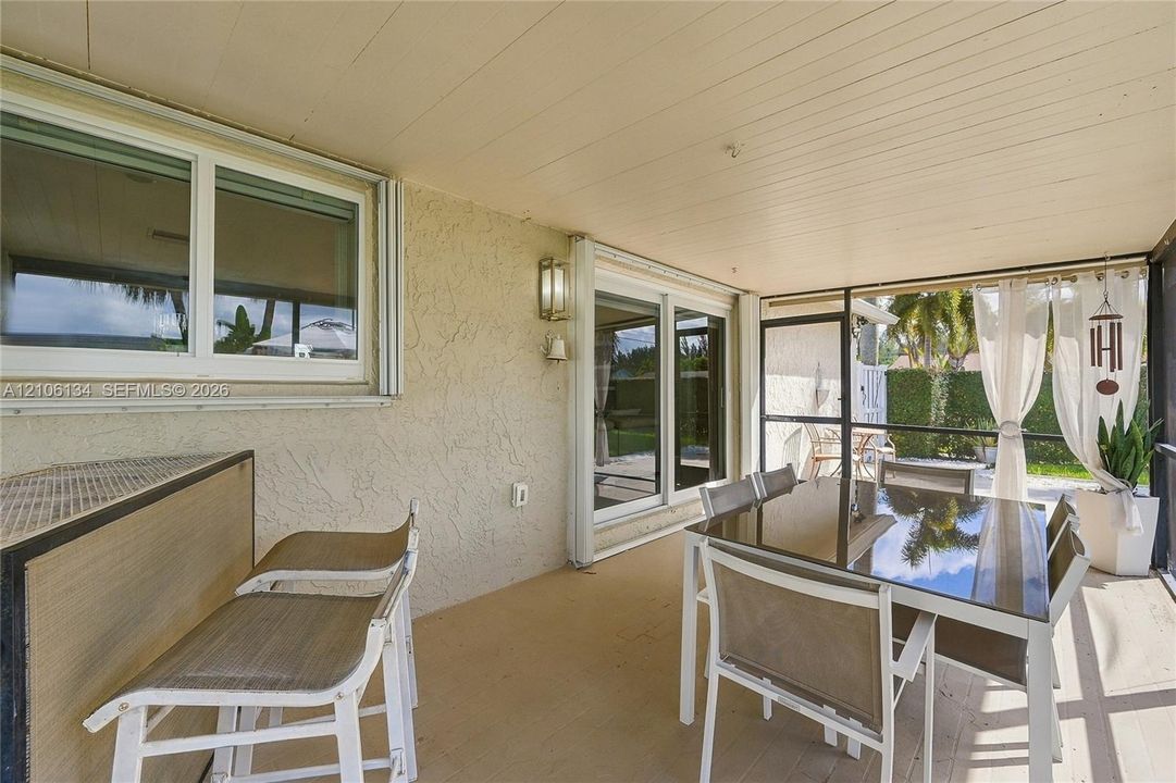 Covered lanai featuring a textured stucco finish, panelled ceiling, dual sliding glass door entryways, and floor-to-ceiling screen enclosure