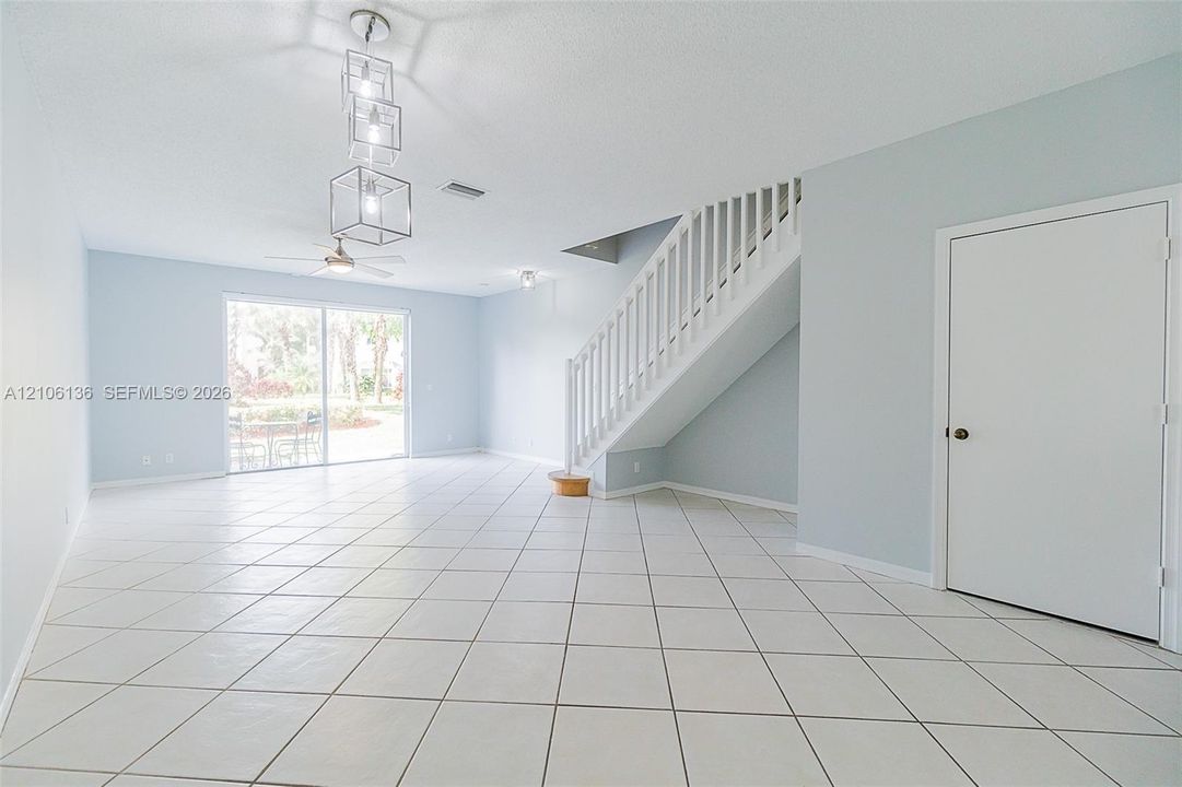 Open-concept interior featuring large-format ceramic tile flooring, a geometric multi-pendant light fixture, a ceiling fan, and a staircase with white vertical railings