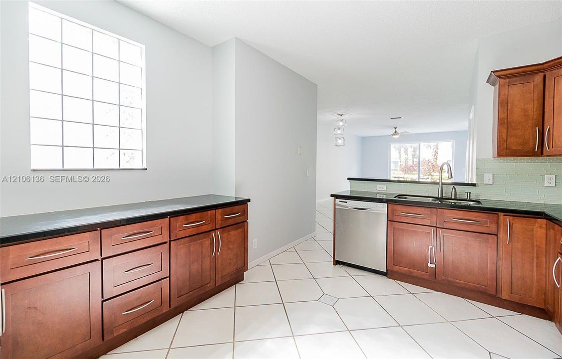 Kitchen featuring wood cabinetry, dark stone countertops, stainless steel dishwasher, glass-block window, and tile flooring