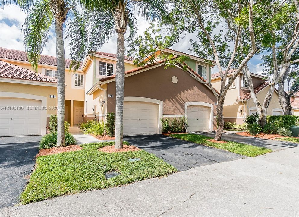 Stucco exterior featuring multi-toned facade, red tile roof, multi-car garage configuration, and manicured landscaping with mature palm trees