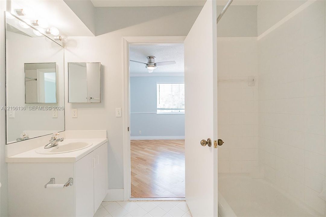 Bathroom featuring a white vanity cabinet with an integrated sink, large wall-mounted mirror, white ceramic tile shower surround, and tile flooring