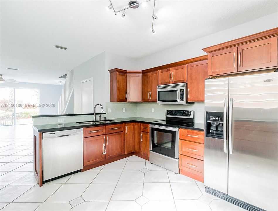 Kitchen featuring wood cabinetry, stainless steel appliances, dark countertops, a double-basin sink, and tile flooring