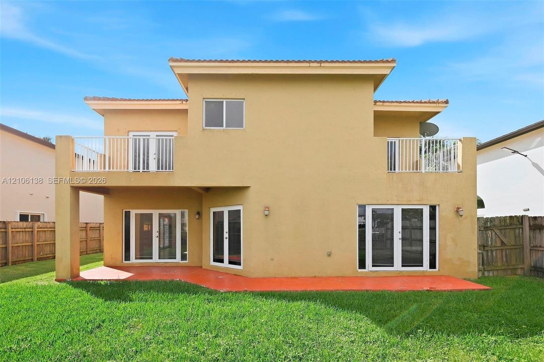 Two-story exterior featuring a stucco facade, covered patio, upper-level balcony with metal railing, and multiple sets of glass-paned doors