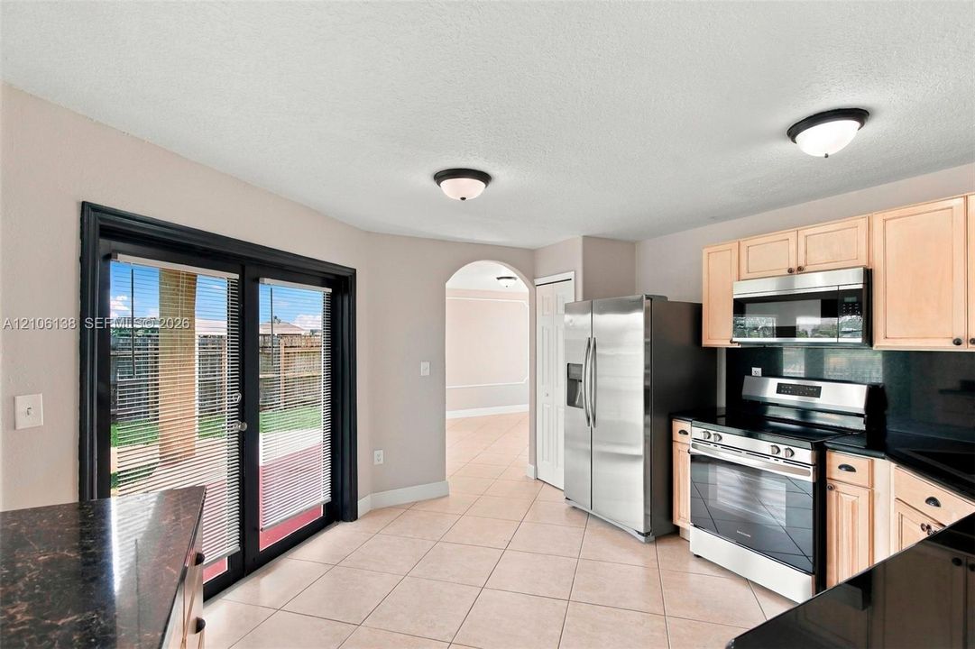 Kitchen featuring light-finish cabinetry, black stone-patterned countertops, stainless steel appliances, ceramic tile flooring, and sliding glass doors